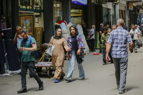 Anadolu via Getty Images Several people walk on the streets of Tehran on a shaded street in July.