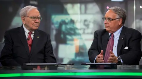 Getty Images Warren Buffett listens as his son Howard Buffett speaks during an interview in New York on 22 October 2013.