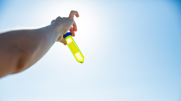 A hand holding a vial of algae up to the sky