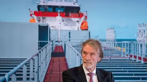 AFP via Getty Images Head and shoulders of a bearded man in suit and tie standing on a ship's gangplank or walkway