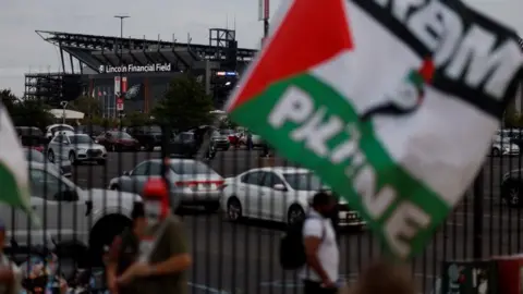 Reuters A few protestors, one waving a large flag with Palestinian colours of white, black, green and red, stand near a parking lot next to Lincoln Financial Field.