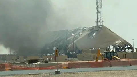 CBS News Undated photo shows smoke billowing from a structure that sustained damage in an Iranian strike at Camp Buehring, Kuwait.