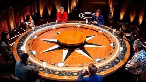 Euan Cherry/Studio Lambert/BBC/Press Association James Acaster, Sebastian Croft, Romesh Ranganathan, Michael Sheen, James Blunt, Kenny Oghenovo Ojuederie (aka King Kenny), Maya Jama and Leigh-Anne Pinnock sit around the iconic roundtable during an episode of The Celebrity Traitors season two.