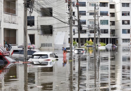 A person wades through flood water between half submerged cars