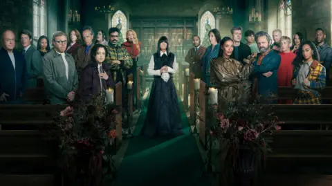 BBC/Studio Lambert/Cody Burridge/BBC Creative The Celebrity Traitors stood in the pews of a church with Claudia Winkelman standing in the middle; they are all smartly dressed