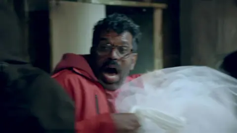 BBC Romesh Ranganathan lets out a scream while holding a dead woman's wedding dress in the haunted cabin