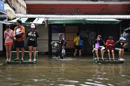 People stand on benches on the flooded pavement