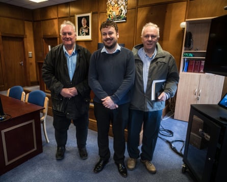 Three Falkland Islands assembly members stand smiling together in a wood-panelled office