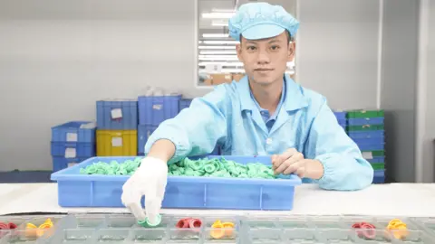 Mihox A worker at the Mihox factory in Dongguan sorting out moulded plastic parts. He is wearing blue overalls and a blue hat