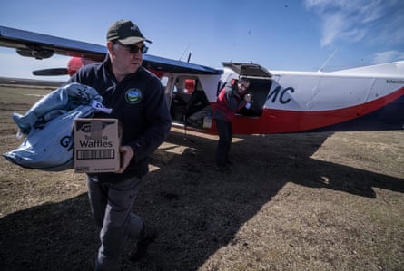 Ricky Evans carries a waffle box and sack past a small plane on Pebble Island