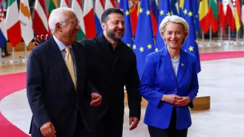 Reuters António Costa, Volodymyr Zelensky and Ursula Von der Leyen laughing as they walk, with many country flags hanging behind them.