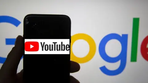 Getty Images An anonymous hand holding a phone showing YouTube, in front of a Google backdrop