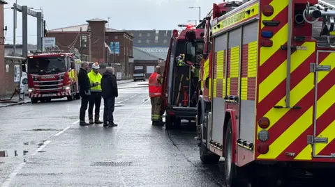 BBC Fire engines parked in a street near the scene of a of a scrap yard fire