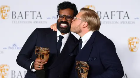 Joe Maher/Getty Images Romesh Ranganathan and Rob Beckett posing at the 2024 Baftas. Rob is kissing Romesh on the cheek