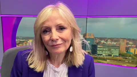 BBC Image show the Mayor of Tracy Brabin wearing a purple jacket with a white blouse. Image in screen behind her is a city scene of Leeds city centre.