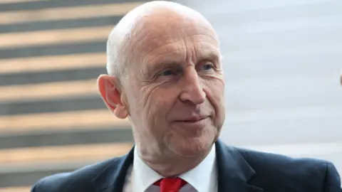Reuters Head and shoulders of John Healey, wearing suit and red tie