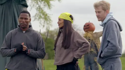 Kenny, Maya and James A stand in front of a scarecrow with a pumpkin's head at the end of Friday's "field of screams" task