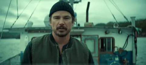 Netflix A production still from the show that depicts Josh Hartnett looking at camera on the deck of a small fishing boat against a moody cloudy grey sky.